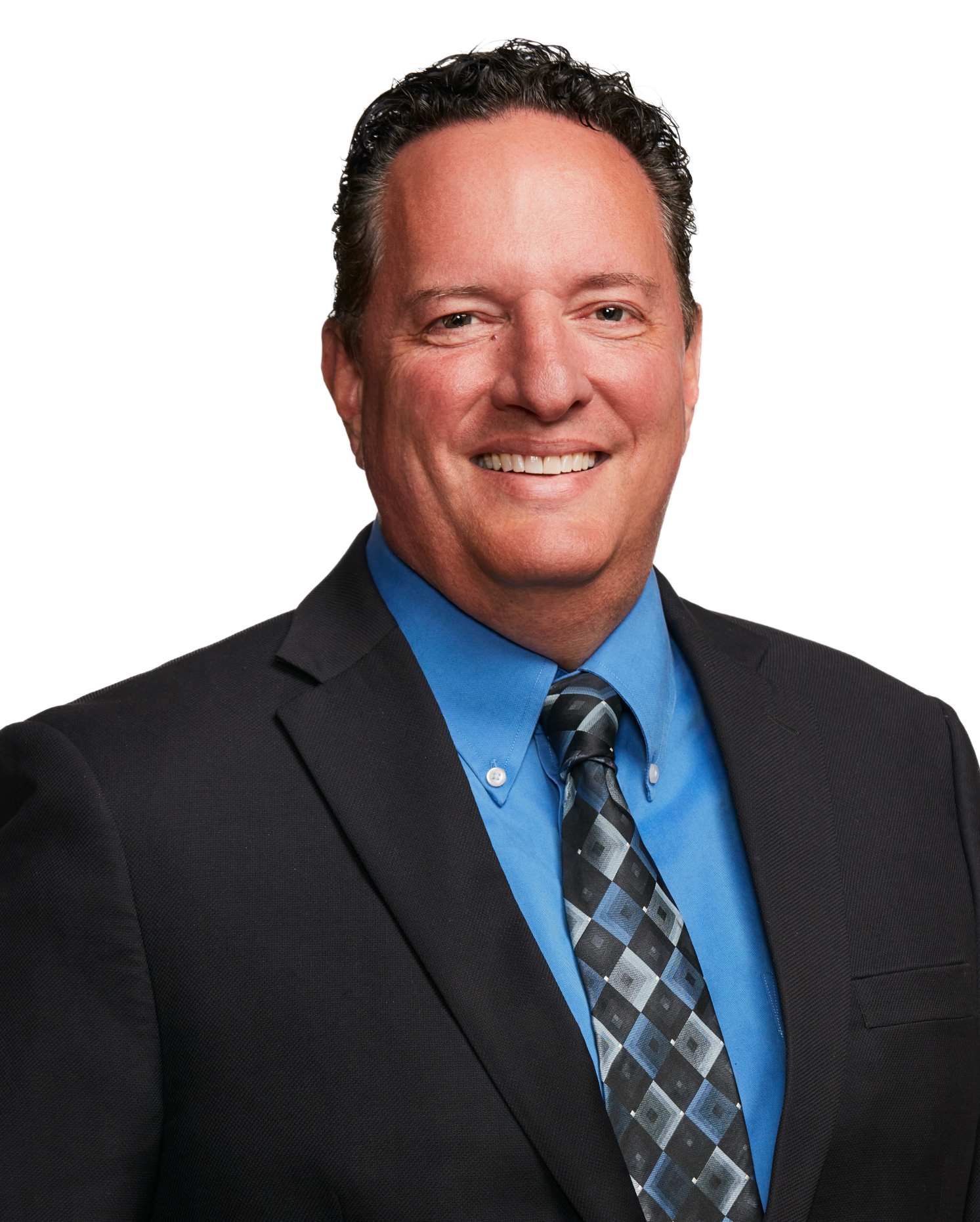 Man with dark hair, tan skin wearing dark suit, blue shirt and tie is smiling